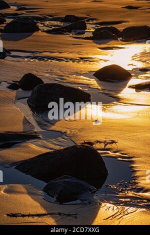 An diesem felsigen Strand erstrahlen bei Sonnenuntergang goldene Farben Stockfoto