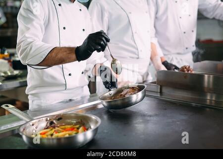 Köche in Schutzmasken und Handschuhen bereiten Essen in der Küche eines Restaurants oder Hotels zu. Stockfoto