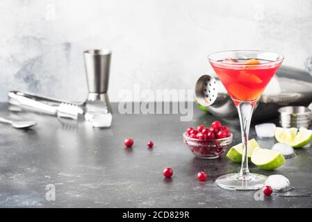 Klassischer alkoholischer Cocktail Cosmopolitan mit Wodka, Likör, Preiselbeersaft, Limette, Eis und Orangenschale, grauer Thekenhintergrund, Barkeeper-Tols, Stockfoto