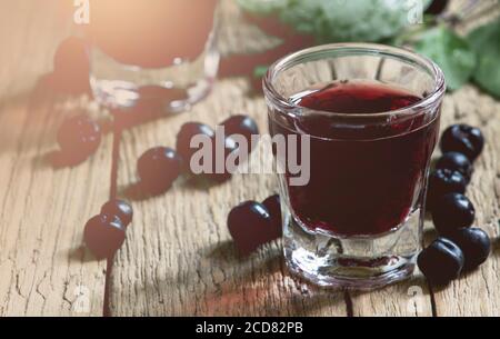 Hausgemachter Aronia-Likör mit frischen Beeren auf altem Holztisch, selektiver Fokus Stockfoto