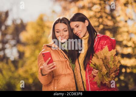 Portrait von zwei schöne attraktive ziemlich fröhlich Freundinnen verbringen Wochenende Oktober hält in den Händen Büschel Baum Blätter umarmen Gerät Gadget Stockfoto
