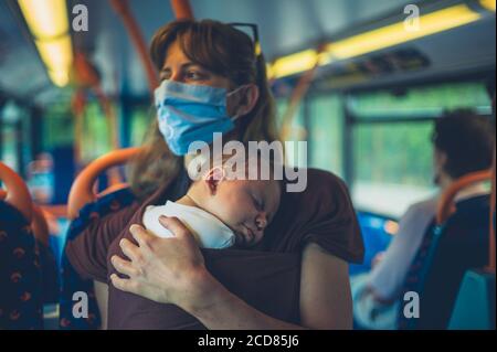 Eine junge Mutter mit ihrem Baby in einer Schlinge ist Tragen einer Gesichtsmaske auf dem Bus Stockfoto