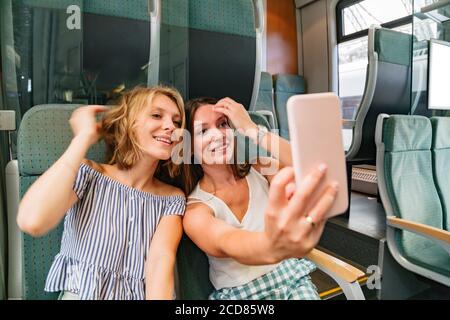 Zwei lächelnde Freundinnen im Zug nehmen Selfies Stockfoto