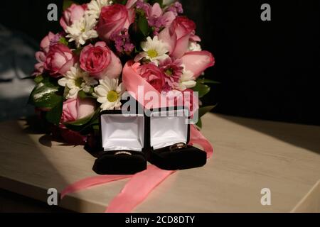 Eheringe in einer schwarzen Box und einem Bouquet von rosen und Gänseblümchen auf einem Holztisch Stockfoto