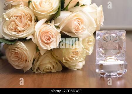 Ein Bouquet von weißen Rosen und eine Kristallbox mit Eheringe auf einem Holztisch Stockfoto