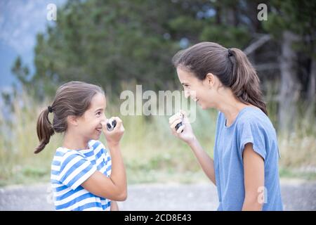 Zwei glückliche Schwestern sehr nahe reden und scherzen mit einem Walkie-Talkie Stockfoto