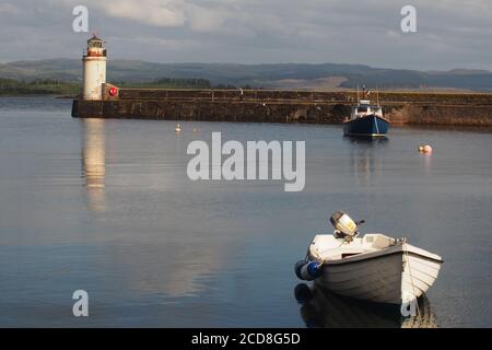 Blick auf den Ardrishaig Pier, Argyll, Schottland mit dem Leuchtturm am Ende und einem kleinen Fischerboot und Ruderboot, das in den ruhigen Gewässern festgemacht ist Stockfoto