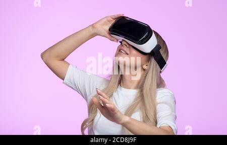 Studio Portrait von glücklichen Frau mit VR-Headset, suchen nach oben, versuchen, Objekte in der virtuellen Realität berühren. Lächelnde Frau beobachten mit VR-Gerät, gesti Stockfoto