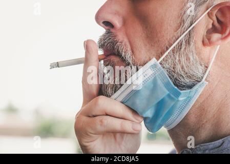 Covid-19, Nahaufnahme eines Mannes mit medizinischer Maske, der eine Zigarette raucht Die Straße Stockfoto