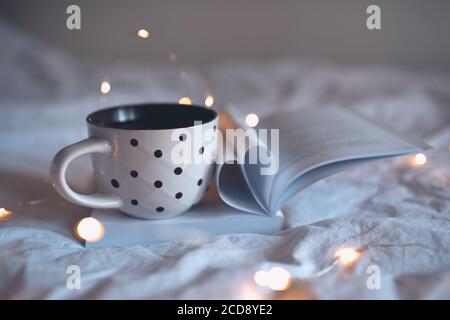 Tasse Tee auf offenem Buch mit herzförmigen gefalteten Seiten in der Nähe im Bett in der Nacht. Herbstsaison. Stockfoto