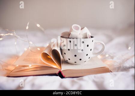 Tasse Kaffee mit Marshmallow auf offenem Buch und gefalteten Seiten in Herzform Nahaufnahme. Wintersaison. Stockfoto
