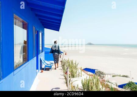 Marocco, Oued Ed-Dahab, Dakhla, Dakhla Attitude Resort, junge Frau auf der Terrasse eines Hotelzimmers mit Blick auf eine Bucht bei Ebbe Stockfoto