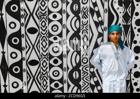 Marocco, Oued Ed-Dahab, Dakhla, Les Dunes Eco-Lodge, junger Marokkaner in traditioneller Kleidung vor einem Zelt mit afrikanischen Stammesmustern Stockfoto