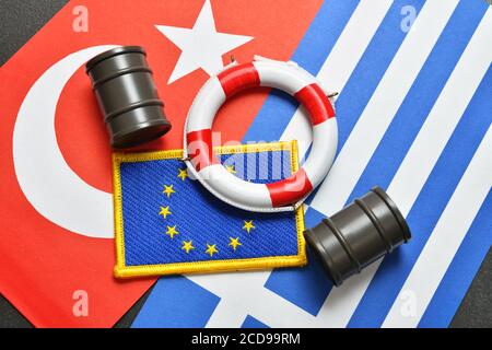 Die Flaggen der Türkei, Griechenlands und der EU mit Rettungsboje und Ölfässer, ägäischer Streit Stockfoto