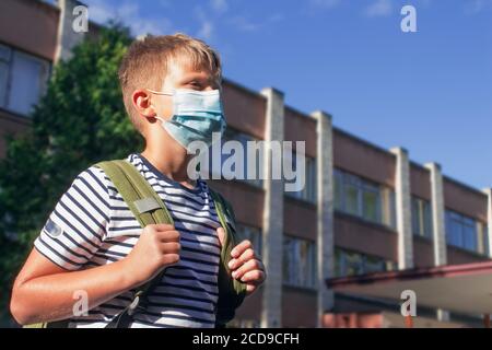 Junge trägt schützende Einweg-Gesichtsmaske, vor dem Schulgebäude stehen. Zurück in die Schule oder Pandemievorsorge Konzept Stockfoto