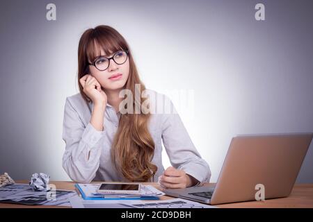 Junge asiatische Bürofrau an einem modernen Schreibtisch, mit Laptop arbeiten, keine Konzentration mit Job, fühlen sich langweilig Stockfoto