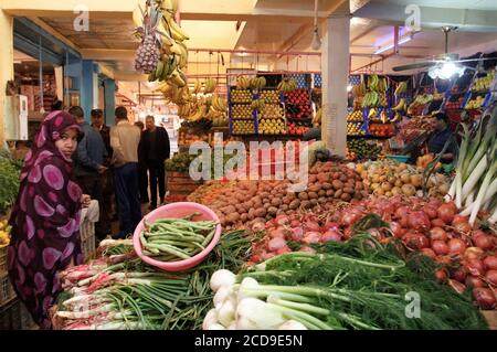 Marokko, Westsahara, Dakhla, saharauische junge Frau, die den traditionellen Schleier vor einem Markt mit Obst und Gemüse trägt Stockfoto