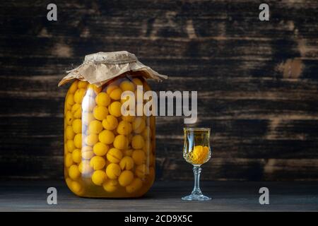 Hausgemachte Tinktur von gelben Kirsche Pflaume im Glas und ein Weinkristall Glas auf Holzhintergrund, Ukraine, Nahaufnahme. Berry alkoholische Getränke Konzept Stockfoto