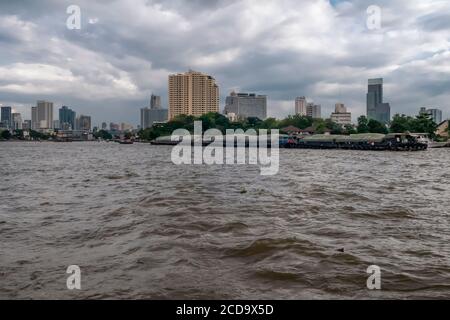 Eine lange Barge segelt auf dem Chao Phraya River in der Innenstadt von Bangkok, Thailand gegen einen dramatischen Himmel Stockfoto