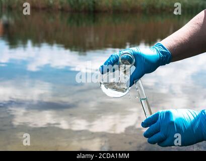 Analyse des Wassers aus dem Fluss auf Verschmutzung. Hand in einem blauen Handschuh hält ein Reagenzglas. Das Konzept der Umweltverschmutzung, Ökologie Stockfoto