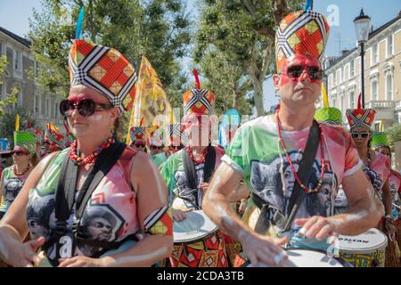 Gruppe von Musikern in bunten Kostümen mit Handtrommeln zu Beginn der Notting Hill Carnival Parade 2019 gesehen. Stockfoto