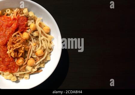 Berühmte traditionelle arabische, ägyptische Gericht - Koshari. National Kushari in einer weißen Platte auf dunklem Holzhintergrund mit Kopierraum. Flach liegend, Draufsicht. Stockfoto