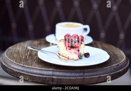 Patisserie-Konzept. Käsekuchen mit Beeren und Kaffee auf Holztisch, Nahaufnahme. Ein Stück Kuchen mit Brombeeren und Himbeeren in der Nähe von Heißgetränk. Köstliches Dessert auf braunem strukturiertem Hintergrund Stockfoto