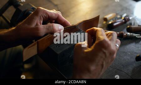 Mann näht Lederdetails in Schraubstock geklemmt. Handwerker arbeitet mit Nadel und Faden. Konzept für kleine Unternehmen. Stockfoto