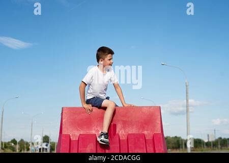 Junge sitzt auf Straßenzaun, Konzept des Spielens auf verbotenes Gebiet Stockfoto
