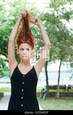 Ginger Mädchen spielt mit ihren Haaren im Park. Frau mit geschädigtem langen Haar. Stockfoto