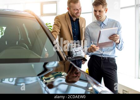 Junge kaukasische Autos Verkäufer sprechen über Vorteile des Autos, empfehlen es dem Kunden. Geschäftsmann, der neue repräsentative Business-Klasse Auto in wählt Stockfoto