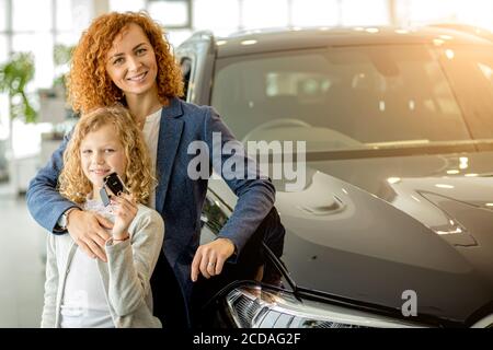 Positive kaukasische Frau und Kind Mädchen in Händler, sie bekam Schlüssel aus dem neuen Auto. Neue Besitzer glänzen mit Glück Stockfoto