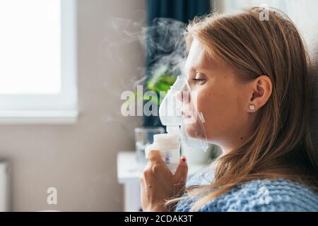 Portrait einer jungen blonden Frau, die zu Hause mit Dampfnebelvernebler inhaliert. Asthma, Grippe, Gesundheitskonzept. Stockfoto