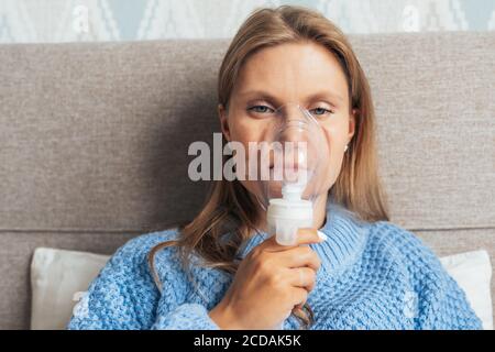 Portrait einer jungen blonden Frau, die zu Hause mit Dampfnebelvernebler inhaliert. Asthma, Grippe, Gesundheitskonzept. Stockfoto