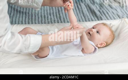 Die Hände der Krankenschwestern machen Gymnastik für ein schönes Baby in einem weißen Bodysuit. Das Baby liegt auf dem Wickeltisch Stockfoto