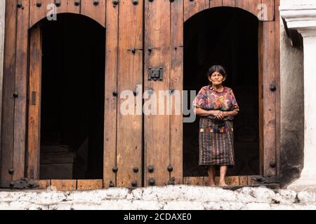 Eine ältere Quiche Maya Frau in traditioneller Kleidung steht in der alten hölzernen Tür der Kirche von Santo Tomas in Chichicastenango, Guatemala. Stockfoto