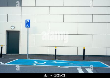 Leerer Behindertenparkplatz mit blauer Markierung und Behinderten-Schild an der Wand. Stockfoto