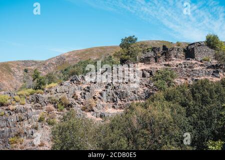 Drave, ein verlassenes Dorf in einem Tal in Arouca, Portugal. Kleine Steinhäuser und weißes Kreuz auf einem Hügel voller Bäume. Stockfoto