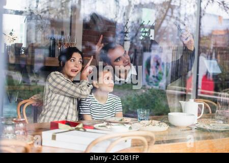 Selfie-Zeit EINE dreiköpfige Familie macht ein Selfie am Küchentisch, macht lustige Gesichter und Gesten. Stockfoto