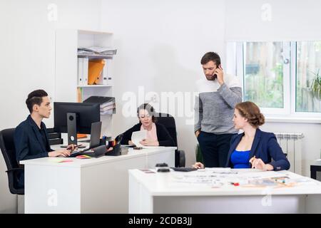 Ein multirassisches Team, das an Computern arbeitet, kommuniziert und in einem Coworking Space kooperiert. Stockfoto