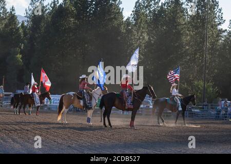 Rodeo-Königinnen und Cowboys präsentieren die Farben während der Eröffnungszeremonie der Kootenai River Stampede in Libby, Montana am Freitag, 24. Juli 2020. Das jährliche Rodeo wurde mit zusätzlichen Sicherheitsmaßnahmen aufgrund steigender COVID-19-Fälle im Bundesstaat abgehalten. Stockfoto