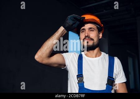 Ein Arbeiter stellt einen orangefarbenen Hut auf seinen Kopf. Er trägt einen Arbeitsanzug Stockfoto