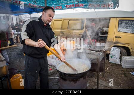 KACAREVO, SERBIEN - 18. FEBRUAR 2017: Mann, der Cvarci in einem Topf auf einem Markt von Kacarevo kocht. Cvarci, oder cvarak, sind typische Schweinefleisch Rinden aus dem Fett von t Stockfoto