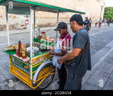 Ein Verkäufer, der Eloten und Ezitate auf der Straße im historischen Zentrum von Oaxaca, Mexiko verkauft. Elotes sind Mais auf dem Kob, die zuerst gekocht werden, dann Stockfoto