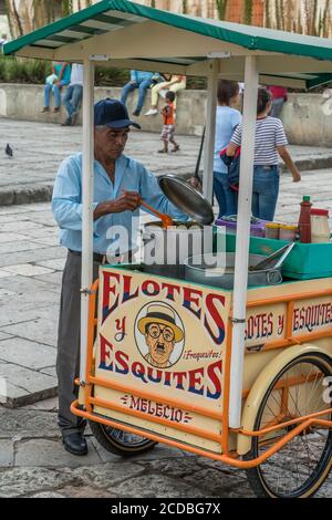 Ein Verkäufer, der Eloten und Ezitate auf der Straße im historischen Zentrum von Oaxaca, Mexiko verkauft. Elotes sind Mais auf dem Kob, die zuerst gekocht werden, dann Stockfoto