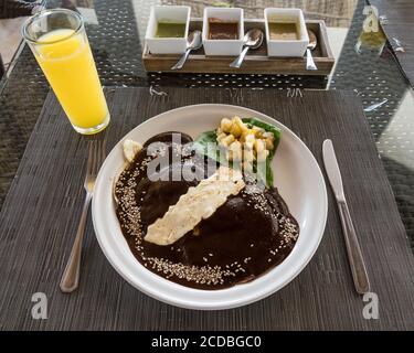 Huevos Oaxaquenos, oder Spiegeleier in schwarzer Maulwurfsauce mit Sesamsamen und geschmolzenem Käse auf einer Maistortilla mit Kartoffeln zum Frühstück in Huatulco, M Stockfoto