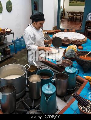 Ein Koch stellt Tortillas in einer Metall-Tortilla-Presse in einem Restaurant in Oaxaca, Mexiko, zu. Vor ihr ist Mais masa Teig aus blau, gelb, und Whi Stockfoto