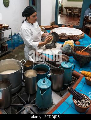 Ein Koch stellt Tortillas in einer Metall-Tortilla-Presse in einem Restaurant in Oaxaca, Mexiko, zu. Vor ihr ist Mais masa Teig aus blau, gelb, und Whi Stockfoto