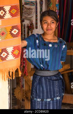 Eine attraktive junge Frau Maya tragen typische Kleid sieht vor die Tür einer Familie Weberei in San Antonio Palopó, Guatemala. Stockfoto