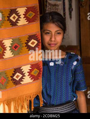 Eine attraktive junge Frau Maya tragen typische Kleid sieht vor die Tür einer Familie Weberei in San Antonio Palopó, Guatemala. Stockfoto